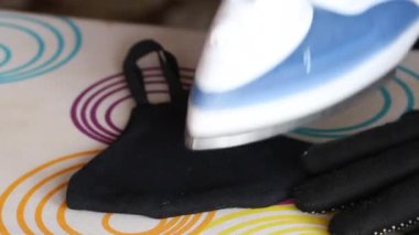 Eldivenli bir adam siyah kumaştan yapılmış yeniden kullanılabilir tıbbi bir maskeyi ütülüyor. Koronavirüs enfeksiyonuna karşı koruma. Yakın çekim.