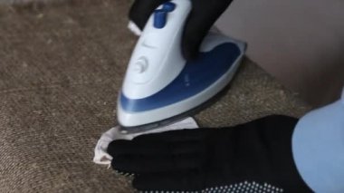 Yeniden kullanılabilir bir tıbbi maske ütüleyen eldiven giyen bir adam. Coronavirus koruması. Yakın çekim..