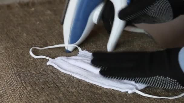 Un hombre con guantes planchando una máscara médica reutilizable. Protección contra el Coronavirus. Primer plano de disparo. — Vídeos de Stock