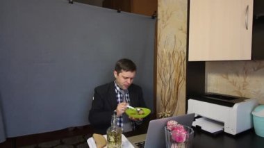 Video görüşmesi sırasında yemek yemek. Takım elbiseli bir adam video iletişimiyle konuşuyor. İletişim kuruyor, tabaktan yiyor..