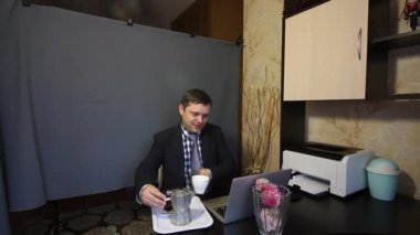 Video görüşmesi sırasında yemek yemek. Takım elbiseli bir adam video iletişimiyle konuşuyor. İletişim kuruyor, yiyor, kahve makinesinden kahve dolduruyor ve bir kekle içki içiyor..