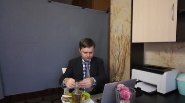 Video görüşmesi sırasında yemek yemek. Takım elbiseli bir adam video iletişimiyle konuşuyor. Bu süreçte, yiyecek alıyor..