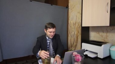 Video görüşmesi sırasında yemek yemek. Takım elbiseli bir adam video iletişimiyle konuşuyor. Bardağa alkol döker. Yakınlarda bir tepside yemek var..