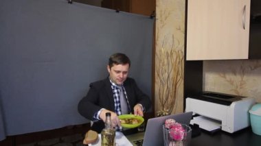Video görüşmesi sırasında yemek yemek. Takım elbiseli bir adam video iletişimiyle konuşuyor. Yemeğini bir tabakta kameraya gösteriyor..