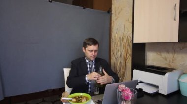 Video görüşmesi sırasında yemek yemek. Takım elbiseli bir adam video bağlantısı üzerinden konuşuyor. RBMC 'ye alkol ve içki döker. Onun yanındaki tepside yemek var..