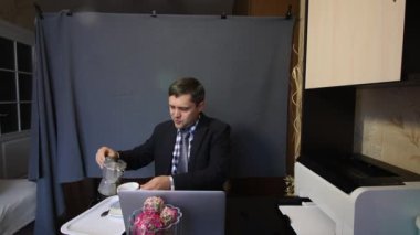 Video görüşmesi sırasında yemek yemek. Takım elbiseli bir adam video iletişimiyle konuşuyor. İletişim kurarken kahve ve jestler yapar..