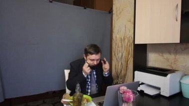 Video görüşmesi sırasında yemek yemek. Takım elbiseli bir adam koruyucu maskeyi yüzünden çıkarıp video iletişimine başlıyor. Kameraya bir şişe alkol gösteriyor. Tepside yiyecek bir şeyler var.