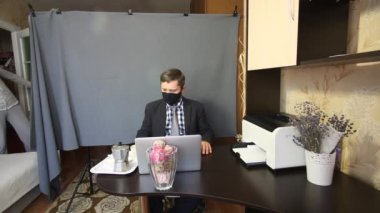 Video görüşmesi sırasında yemek yemek. Maskeli ve takım elbiseli bir adam video iletişimiyle konuşuyor. Bir kadın dikkatini dağıtıyor. Konuşmaya ve kahve içmeye devam ediyor..