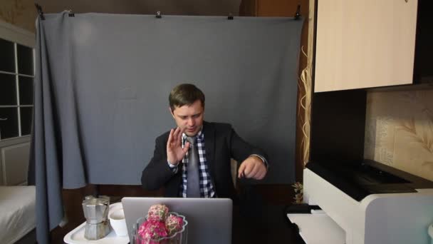 Eating during a video call. A man in a business suit removes the mask from his face and talks via video link. While communicating, he drinks coffee and gestures. Nearby on a tray is a coffee maker and — Stock Video