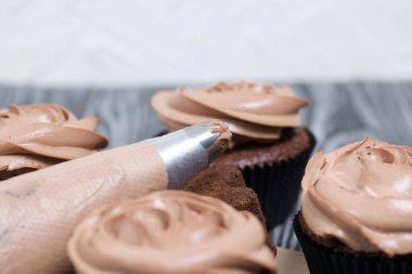 Krem peynirli çikolatalı kekler. Yanında süsleme için kremalı bir pasta torbası var..