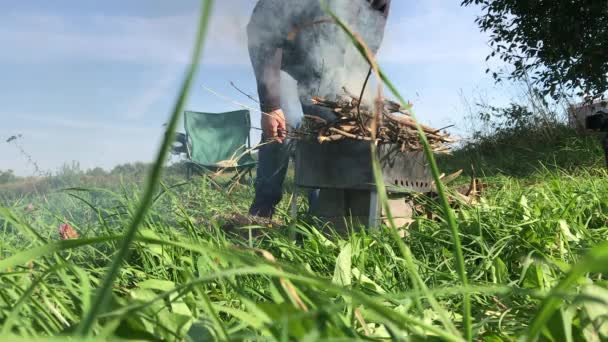 한 남자가 브러시 우드를 금속 버저에 올려 놓는다. 연기가 나는 곳이지. 세계적 유행병이 휩쓸고 있는 초원에서의 피크닉. — 비디오