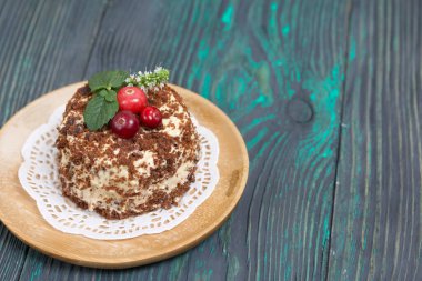 Tereyağlı kremalı pandispanya. Kızılcık ve nane ile süslenmiş. Fırçalanmış çam ağaçlarının arka planında.