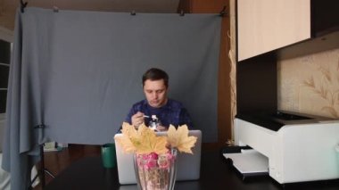 Bir adam bilgisayarın önündeki masada otururken video iletişimiyle iletişim kuruyor. Tatlıyla kahve içer. Arkasında gri bir arka plan örtüsü var. Konuşmayı bitirir, kapanır