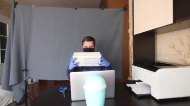 Maskeli ve eldivenli bir adam, bir dizüstü bilgisayarın önünde masada otururken video iletişimiyle iletişim kuruyor. Alınan paketi kamerada gösteriyor ve büro bıçağıyla açıyor. Gergin 