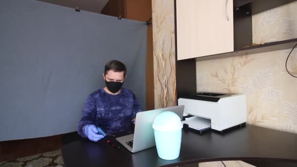 Ein Mann mit Maske und Handschuhen kommuniziert per Videoübertragung, während er an einem Tisch vor einem Laptop sitzt. Er holt einen Brief aus den Umschlägen und liest ihn vor. Hinter ihm liegt ein grauer Rücken — Stockvideo