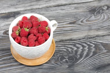 Büyük beyaz bir kupada ahududu. Ahşap tahtaların üzerinde güzel bir dokusu var..