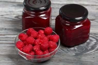 Cam kavanozlarda ahududu reçeli. Yakınlarda bir konteynırda ahududu var. Ahşap tahtaların üzerinde güzel bir dokusu var..