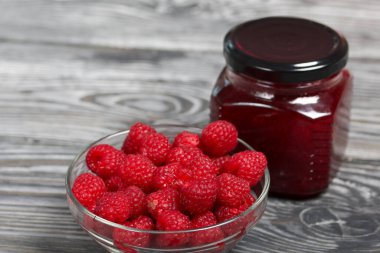 Cam kavanozlarda ahududu reçeli. Yakınlarda bir konteynırda ahududu var. Ahşap tahtaların üzerinde güzel bir dokusu var..