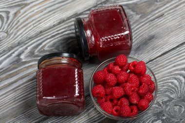 Cam kavanozlarda ahududu reçeli. Yakınlarda bir konteynırda ahududu var. Ahşap tahtaların üzerinde güzel bir dokusu var..