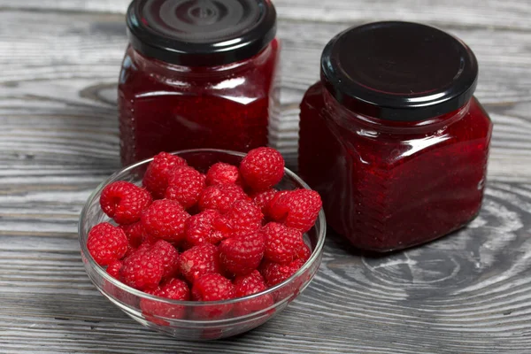 Cam kavanozlarda ahududu reçeli. Yakınlarda bir konteynırda ahududu var. Ahşap tahtaların üzerinde güzel bir dokusu var..