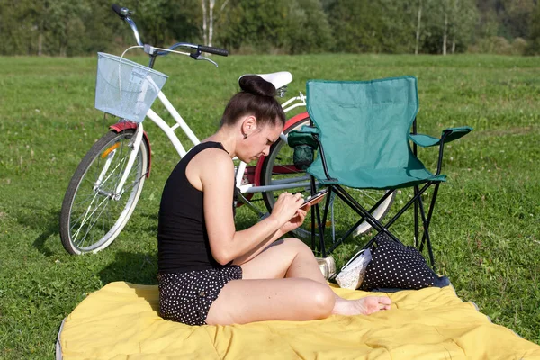 Dziewczyna Odpoczywa Parku Siedzi Dywanie Patrzy Telefon Pobliżu Znajduje Się — Zdjęcie stockowe