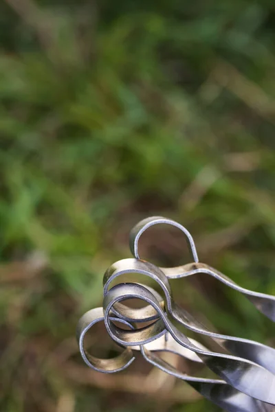 Handles of metal skewers. Bent in a spiral. With a ring at the end. Against the background of green grass.