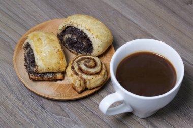Haşhaş ve tarçınla doldurulmuş çörek. Tabağa uzan. Yakınlarda bir fincan kahve var..