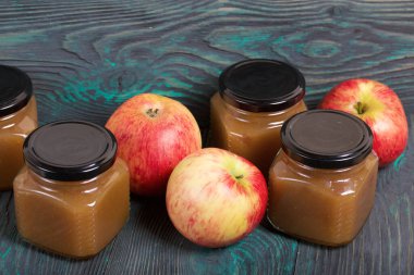 Kavanozda elma reçeli. Yakınlarda olgun elmalar var. Fırçalanmış tahtalarda, siyah beyaz boyanmış..