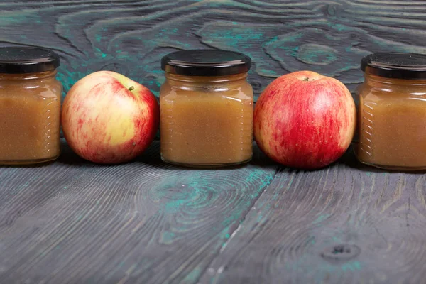 Apple jam in jars. Nearby are ripe apples. On brushed boards, painted black and white.
