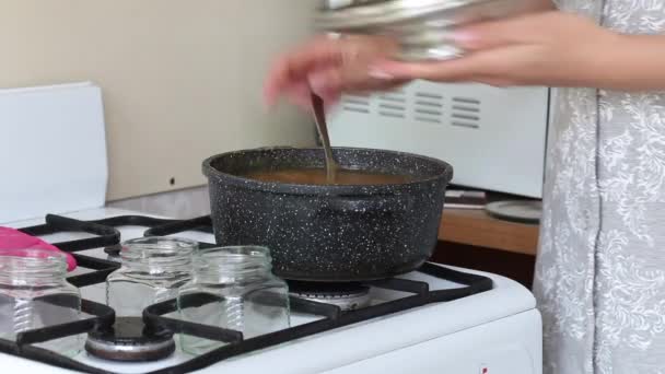 La femme fait de la confiture de pommes. Mélanger avec une cuillère dans une casserole. Endroits dans des bocaux en verre. — Video