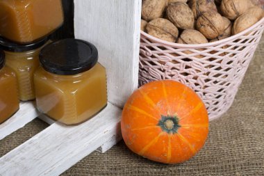 Kavanozda meyve reçeli. Beyaza boyanmış ahşap bir kutuda duruyor. Yanında bir sepet ceviz ve turuncu balkabağı var..