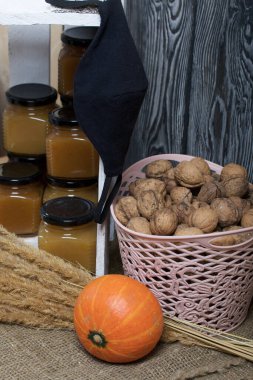 Kavanozda meyve reçeli. Beyaza boyanmış ahşap bir kutuda duruyor. Yanında bir sepet ceviz, bir portakal kabağı ve bir buket kuru ot var. Bir tıbbi maske sallanıyor..