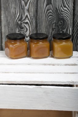 Kavanozda meyve reçeli. Beyaz boyalı ahşap bir kutunun üzerinde duruyor. Siyah çam ağaçlarının arka planında.