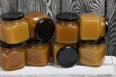 Kavanozda meyve reçeli. Beyaz boyalı ahşap bir kutunun üzerinde duruyor. Siyah çam ağaçlarının arka planında.