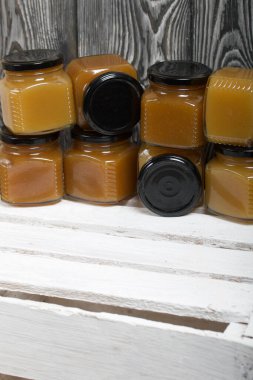 Kavanozda meyve reçeli. Beyaz boyalı ahşap bir kutunun üzerinde duruyor. Siyah çam ağaçlarının arka planında.