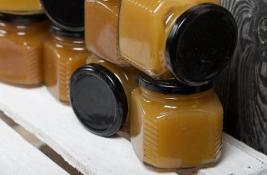 Kavanozda meyve reçeli. Beyaz boyalı ahşap bir kutunun üzerinde duruyor. Siyah çam ağaçlarının arka planında.