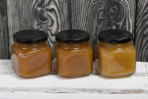 Fruit jam in jars. Stands on a white-painted wooden box. Against the background of black pine boards.