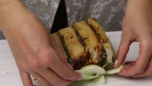 A piece of bacon, cut into an accordion. Filled with parsley and adjika. The woman puts it on chopped onion and wraps it in plastic wrap. Salted lard with herbs and spices. — Stock Video