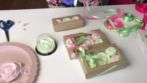 Eine Frau packt rosa und hellgrüne Marshmallows in Geschenkkartons. Bindet sie mit einer Schleife zusammen. — Stockvideo
