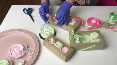 Bir kadın hediye kutusuna pembe ve açık yeşil zephyr koyar. Bir kurdele ve papyonla bağlar.