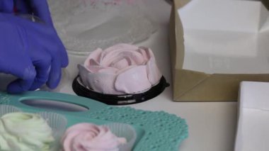 Bir kadın plastik bir kapta pembe gül şeklinde bir zephyr taşıyor. Paketleme için yakın aksesuarlar.