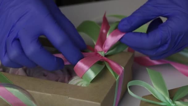 Una mujer está atando una cinta en zephyr, embalada en cajas de cartón de regalo. Ata una cinta en un lazo. — Vídeo de stock