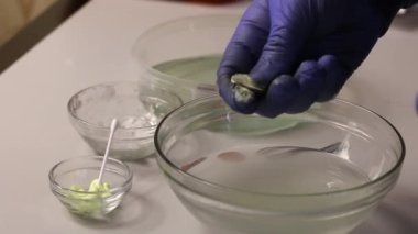 Lastik eldivenli bir adam sikkeye sülfür merhemi sürer. Bir madeni parayı sıcak suya sürter. Sülfürik merhemle bakır paraların şekli. Yakın plan..