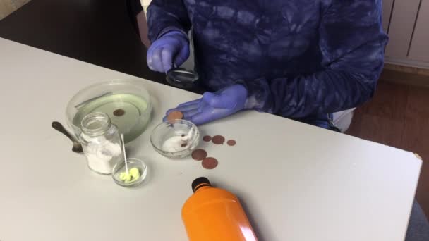 A masked man with rubber gloves puts a copper coin in phosphoric acid. Rubs another coin with soda. Nearby is a sulfuric ointment for cleaning copper coins. — Stock Video