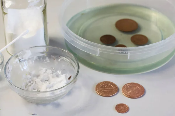 Peeled copper coins lie on the table surface. Corroded coins are lying nearby in a container with phosphoric acid.