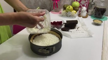 Bir kadın çikolatalı ganache ve fırında bisküvi üzerine hindistan cevizi taneleri koyar. Levington Turtası Pişirme.