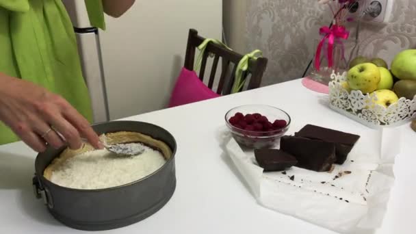 Una donna mette dei fiocchi di cocco su una ganache al cioccolato e un biscotto al forno. Nelle vicinanze lamponi e cioccolato. Cottura Levington Pie. — Video Stock