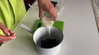 Bir kadın tencerede çikolataya süt döküyor. Levington turtası için ganache yapar.