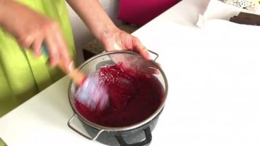 Bir kadın elek aracılığıyla ahududu reçeli öğütüyor. Levington Turtası Pişirme.