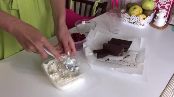 Une femme mélange noix de coco, sucre et lait. Chocolat et framboises à proximité. Cuisson Levington Tarte. — Video